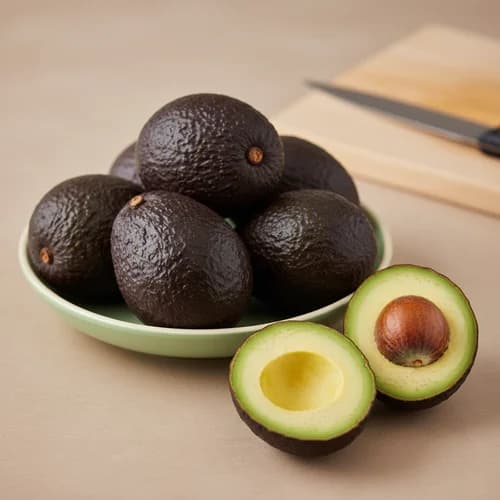 Avocado interi in una ciotola verde accanto a un avocado tagliato a metà con nocciolo.
